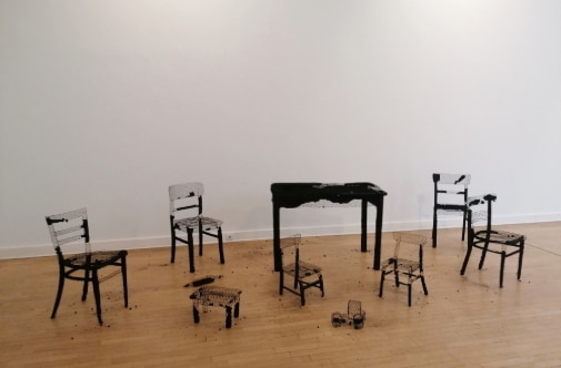 Conceptual installation with chairs and table in an exhibition setting.